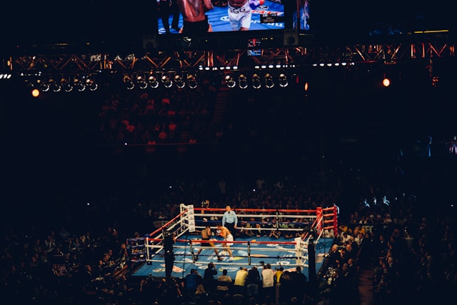 A photo of a two fighters in a boxing ring from a distance, with a crowd watching.
